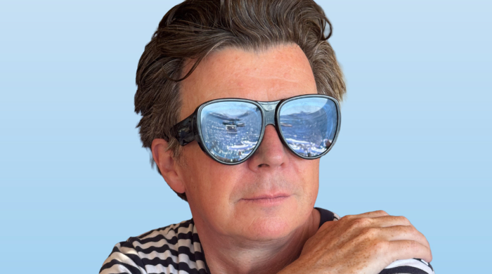 Musician Rick Astley wearing sunglasses which reflect a crowd.